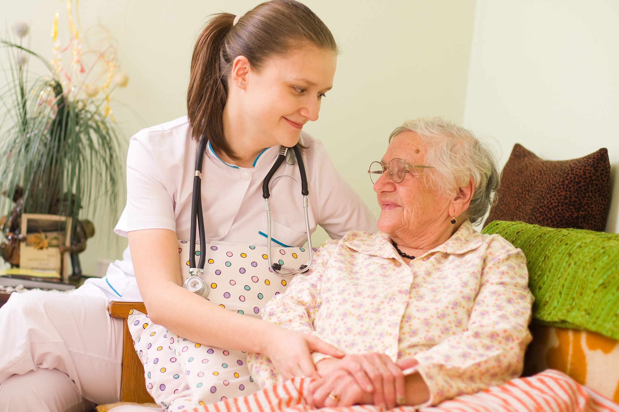A nurse attentively listens and smiles while holding hands with an elderly patient, showcasing compassionate healthcare in a cozy setting.